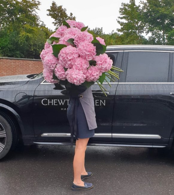Woman carrying a bouquet of flowers outside of a Chewton Glen branded car.